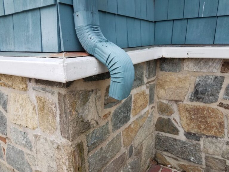 Painted Blue Drainspout Along Blue Siding and Stone