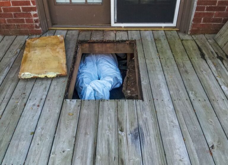 Man in Protective Suit Crawling in Crawl Space Under House