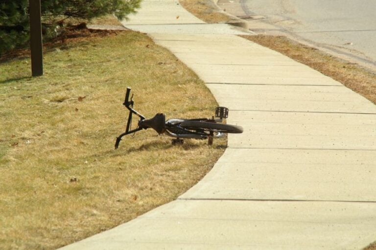 Bike Laying on the Grass Next to a Sidewalk